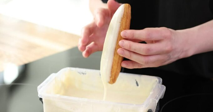 Pastry chef dipping eclair cake into bowl with icing