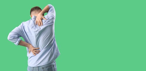 Young man suffering from back pain on green background with space for text