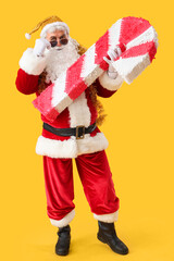 Cool Santa Claus with candy cane pinata on yellow background