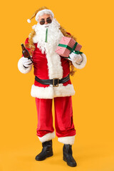 Cool Santa Claus with beer and Christmas gift on yellow background