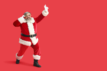 Funny Santa Claus in headphones listening to music and dancing on red background