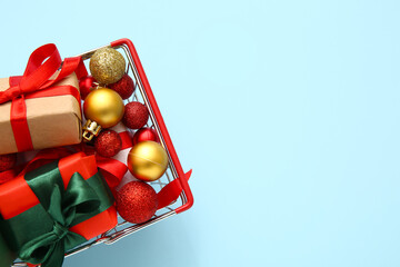 Shopping basket with Christmas balls and gift boxes on blue background