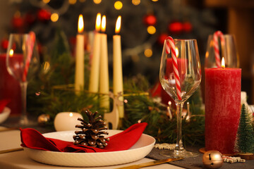 Christmas table setting with burning candles in room at night, closeup