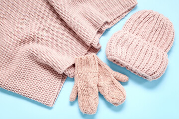 Knitted hat, scarf and mittens on color background