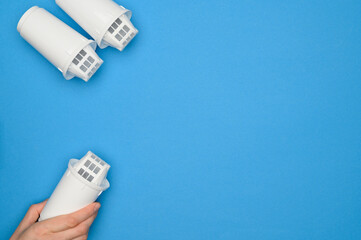 Layout : new filter cartridges for clean water on blue background, one in female hand, top view....