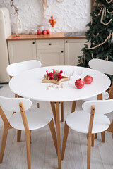 A cozy, festive dining table adorned with red apples and decorative elements, surrounded by elegant white chairs in a warmly decorated home