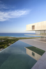 Modern coastal villa with infinity pool overlooking serene ocean at sunset