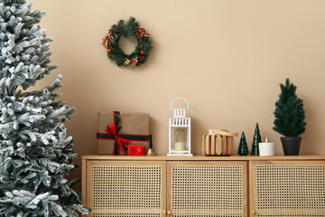 Wooden cabinet with lantern, gift boxes and Christmas decor near beige wall