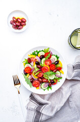 Colorful vegetable salad with olives, tomato, paprika, cucumber, onion, and herbs. White background, top view