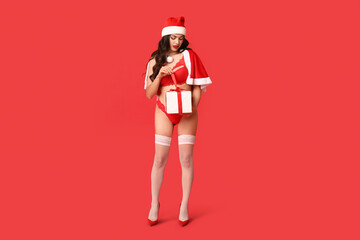Beautiful young sexy woman in lingerie dressed as Santa with gift box on red background