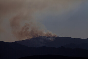 Smoke rising from mountainous wildfire distant plane trailing away