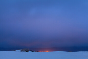 Naklejka premium Distant orange lights against deep blue evening sky