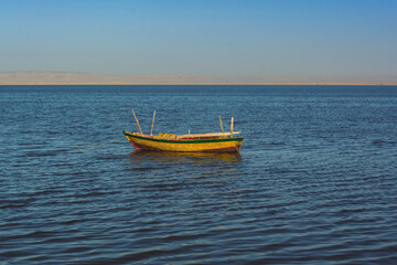 A small colorful boat adrift on a calm sea against blue sky