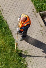 A man in an orange vest is sweeping the sidewalk