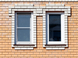 Two windows with white frames sit on a brick wall
