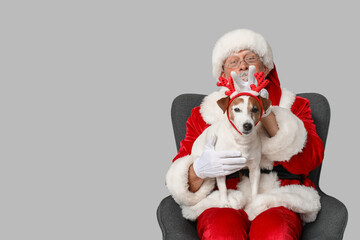 Santa Claus with cute Jack Russell Terrier dog in reindeer horns on grey background