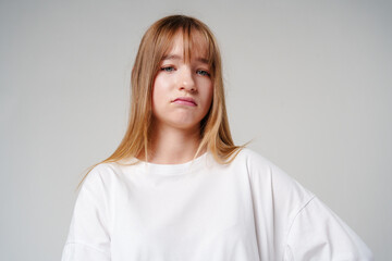 Fototapeta premium A young girl with long hair looks unimpressed against a plain background
