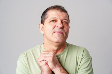 A thoughtful older man expresses gratitude while looking up with hope in a simple green shirt against a light backdrop