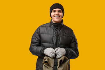 Young man in black stylish puffer jacket and hat with bag on yellow background