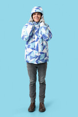 Young man in stylish puffer jacket and gloves on blue background