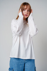 A young woman with long hair hides her face in a white sweater against a plain background