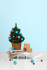 Sledge with Christmas tree in pot and gifts near blue wall