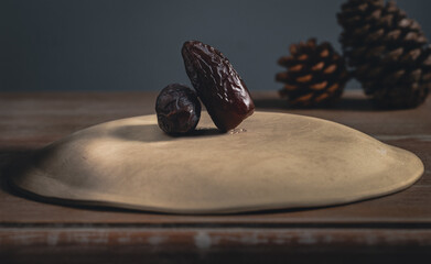 Dried date fruits on a plate with pine cones on a wooden table.