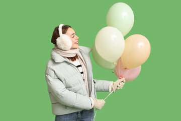 Beautiful young woman in warm winter clothes with balloons on green background