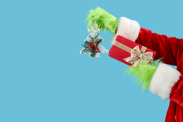 Green hairy hands of creature in Santa costume with decorative fir tree and Christmas gift box on...