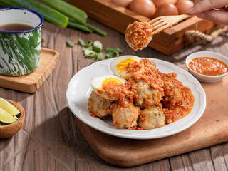 A plate of traditional siomai, a type of Indonesian steamed dumpling served with a spicy peanut sauce and accompanied by hard-boiled eggs. a hand holding a fork is lifting a piece