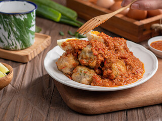 A plate of traditional siomai, a type of Indonesian steamed dumpling served with a spicy peanut sauce and accompanied by hard-boiled eggs. a hand holding a fork is lifting a piece