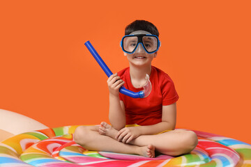 Cute little boy in swimming mask sitting on inflatable mattress on red background