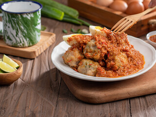 A plate of traditional siomai, a type of Indonesian steamed dumpling served with a spicy peanut sauce and accompanied by hard-boiled eggs. a hand holding a fork is lifting a piece