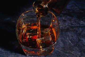Whiskey being poured into a glass with ice on a blue background