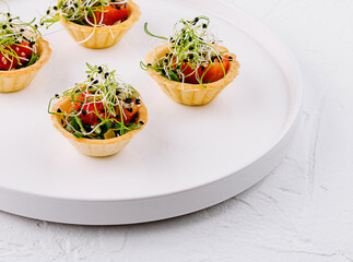 Elegant canapes with juicy tomatoes and delicate microgreens on a white plate