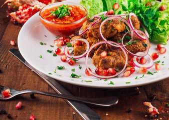 Grilled meat with pomegranate seeds, onion rings and sauce on a white plate, garnished with fresh herbs