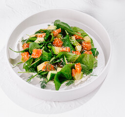Fresh and healthy salad with salmon, avocado and spinach, served on a white plate