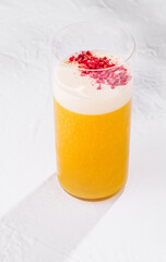 Refreshing yellow cocktail with white foam and raspberry powder topping on white background