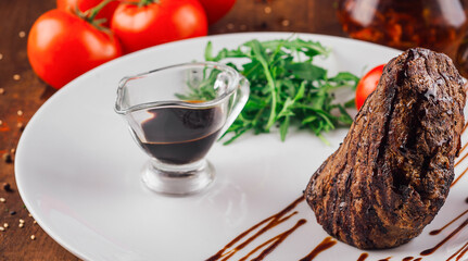 Grilled beef steak with sauce, arugula, tomato and spices on white plate