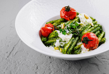 Italian pasta with pesto sauce, tomatoes and burrata cheese being served on white plate
