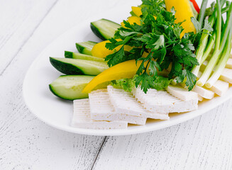 White plate showing sliced cheese with cucumber and green onions on white table