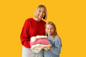 Beautiful woman and her cute daughter in stylish sweaters with clothes on yellow background