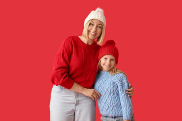 Beautiful woman with her cute daughter in stylish sweaters and hats on red background