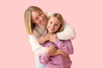 Beautiful woman hugging her cute daughter in stylish sweaters on pink background