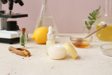 Laboratory glassware and microscope with ingredients for preparing natural cosmetics on white table near pink wall