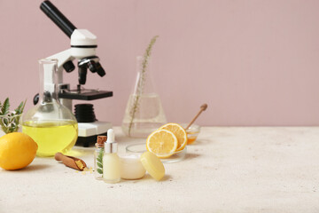 Laboratory glassware and microscope with ingredients for preparing natural cosmetics on white table near pink wall