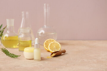 Laboratory glassware with ingredients and samples for preparing natural cosmetics on beige table near pink wall