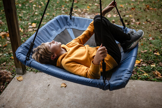 Child in yellow hoodie relaxing on a tree swing outdoors in autumn