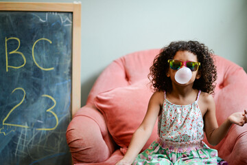 Young girl with sunglasses blowing a bubble with bubblegum, sitt