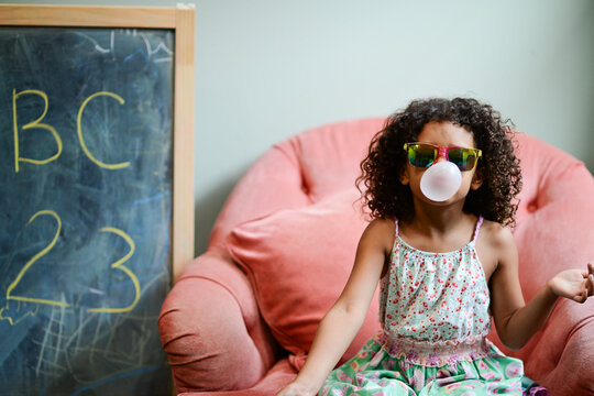 Young girl with sunglasses blowing a bubble with bubblegum, sitt